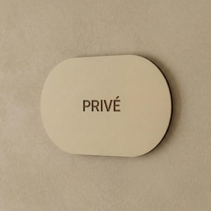 May include: An oval-shaped beige sign with a dark brown border. The word PRIVÉ is centered on the sign in dark brown capital letters. The sign has a smooth, matte finish and a clean, rounded edge design that is consistent throughout the piece.