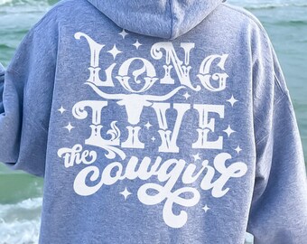 May include: A light gray hoodie with the text "Long Live the Cowgirl" in white script and a longhorn graphic on the back. The hoodie has a hood and is being worn on a beach.