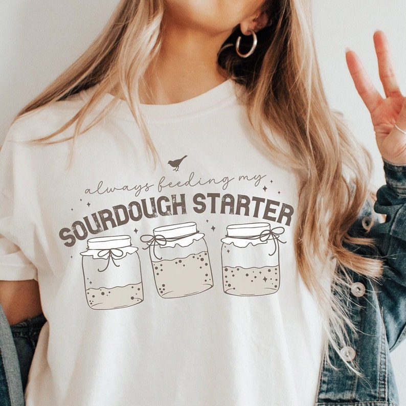 May include: White t-shirt with the text "always feeding my sourdough starter" and a drawing of three jars with sourdough starter inside.