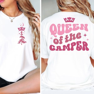 Könnte beinhalten: Weißes T-Shirt mit einem rosa und weißen Design auf Vorder- und Rückseite. Das Design auf der Vorderseite zeigt eine Kiefer mit einer Krone und einem Halbmond darüber. Das Design auf der Rückseite lautet "Queen of the Camper" in einer Retro-Schriftart mit einer Krone über dem Wort "Queen".