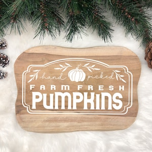 Puede incluir: Un letrero de madera con un diseño pintado en blanco que dice "hand picked farm fresh pumpkins". El letrero es marrón y tiene un aspecto rústico.
