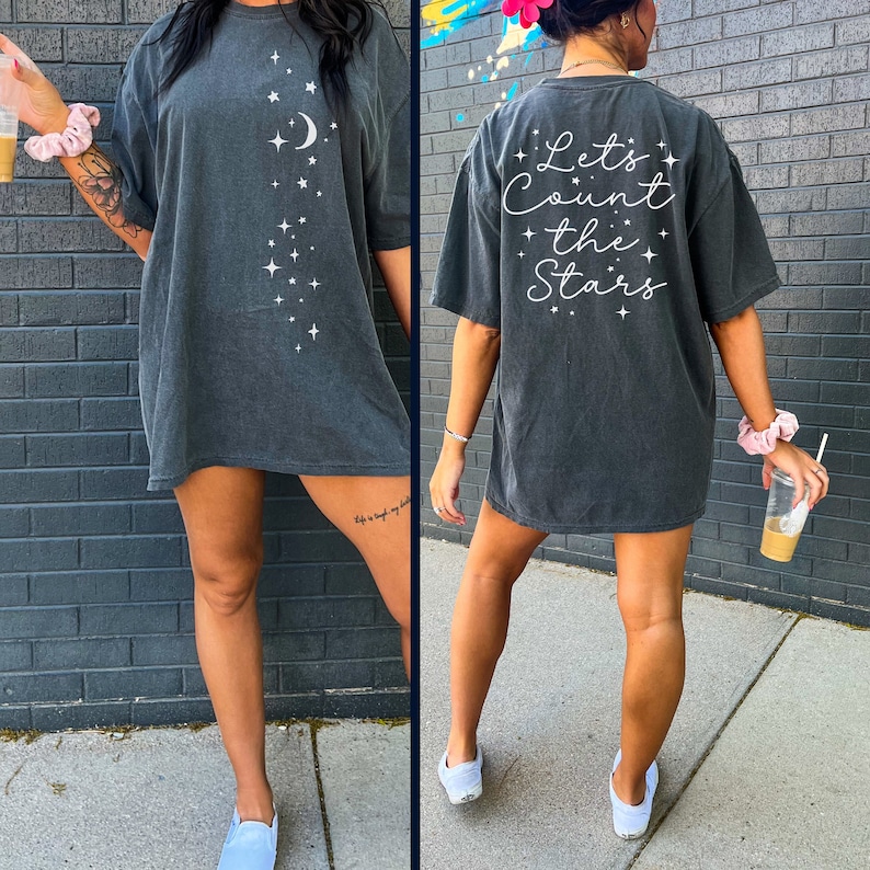 May include: A dark gray oversized t-shirt with a white graphic of stars and a crescent moon. The back of the shirt has the text "Let's Count the Stars" in white.