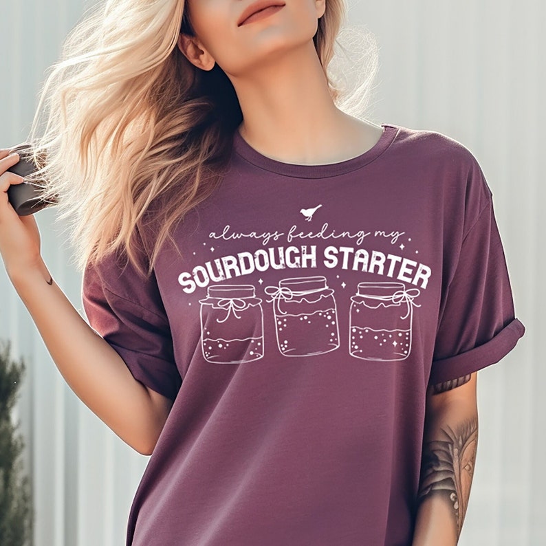May include: A purple t-shirt with the text "always feeding my sourdough starter" and a graphic of three jars with lids and ribbons.