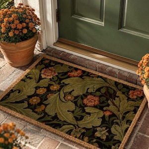 May include: A rectangular doormat featuring a dark background with a repeating pattern of large, light green foliage and orange floral blooms. The mat is positioned on a brick surface in front of a green door, flanked by two terracotta pots.