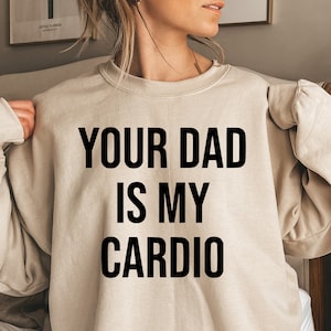 May include: A beige sweatshirt with the text "YOUR DAD IS MY CARDIO" printed in black.