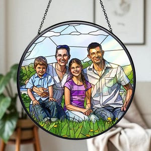 May include: A round, stained-glass window featuring a family portrait. The image shows a family of four, with two parents and two children, sitting in a grassy field. The window is framed in black and hangs from a chain.