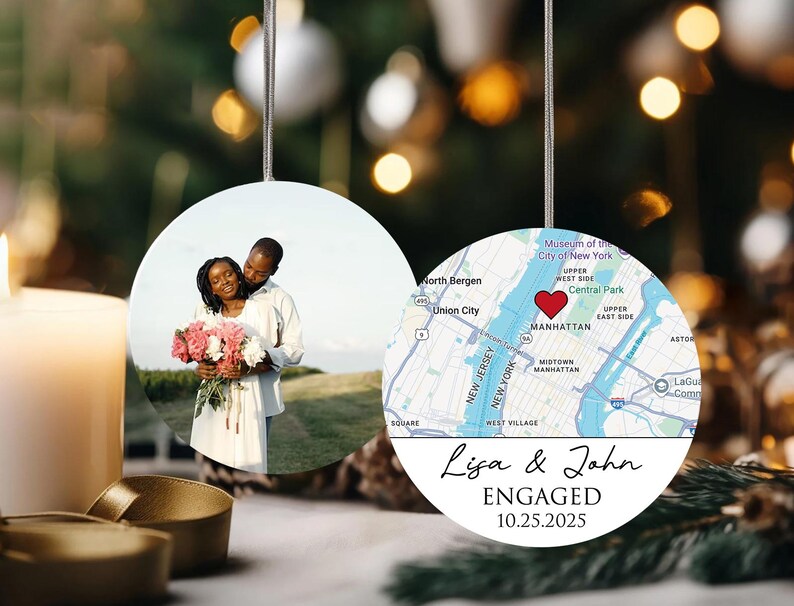 May include: Round ceramic ornament with two sides. One side features a couple holding flowers, the other a map of Manhattan with a heart marking a location. Text reads "Lisa & John ENGAGED 10.25.2025".