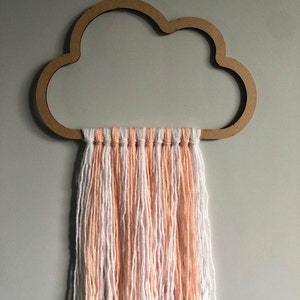 Puede incluir: Una decoración de pared en forma de nube de madera con una franja de hilo de melocotón y blanco.