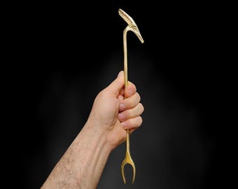 Puede incluir: Un utensilio de metal dorado con forma de pájaro, con un mango largo y delgado y un tenedor de dos puntas en el extremo.