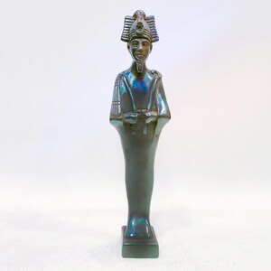 Puede incluir: Una estatua de cerámica verde oscuro de un faraón egipcio con un tocado y una cara detallada. La estatua está de pie sobre una base cuadrada.