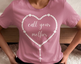 May include: A pink t-shirt with a white heart-shaped rosary design and the text "call your mother" inside the heart.