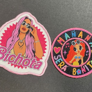 May include: Two embroidered patches. One is a pink and white patch with the word "Bichota" and a pop art style illustration of a woman with pink hair and sunglasses. The other is a circular patch with the words "Mañana Sera Bonito" and a cartoon illustration.