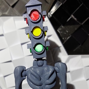 May include: A gray 3D printed figure of a skeleton with a traffic light for a head. The traffic light has red, yellow, and green lights.