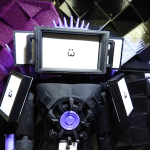 May include: Black and purple 3D printed robot toy with a screen displaying a cartoon face. The robot has a large gear-like design on its chest.