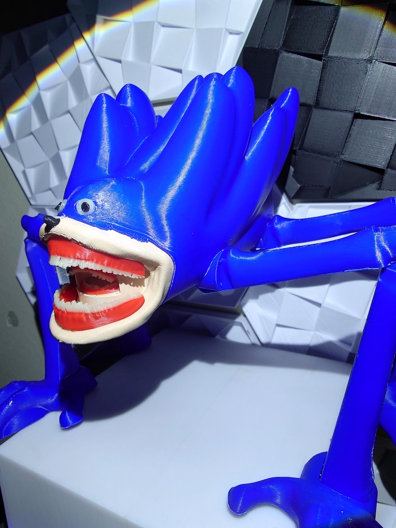 May include: A blue, stylized creature with a large open mouth revealing teeth. The figure has long limbs and a spiky head. The creature is posed on a white surface, with a geometric background of black and white shapes.