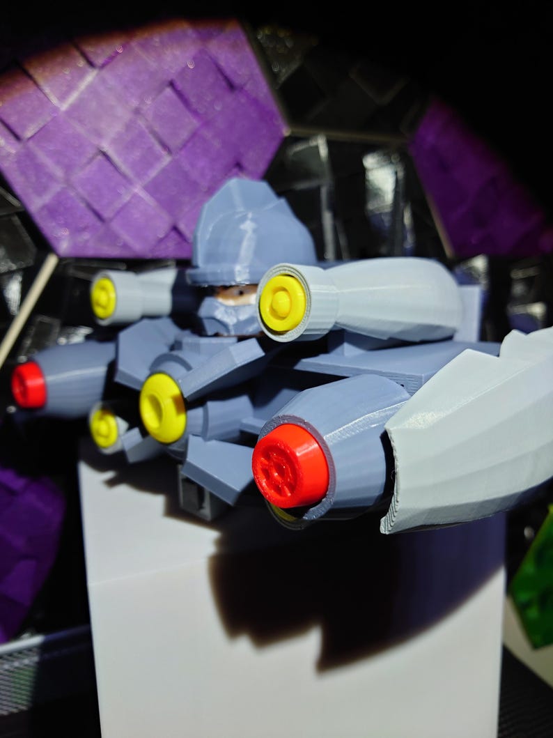 May include: A gray and white robot toy with yellow and red details. The robot has multiple arms and cannons. The robot is posed with its arms extended.