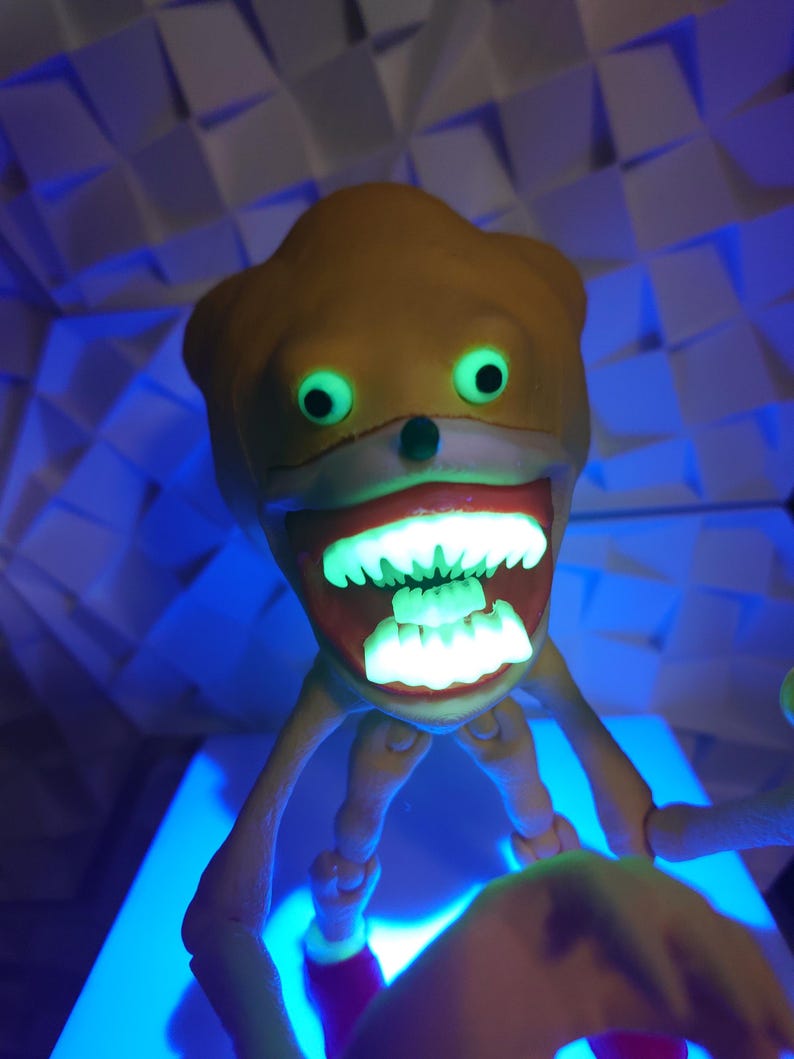 May include: A yellow and white toy with a large toothy grin and glowing green eyes. The toy has long, thin arms and legs.