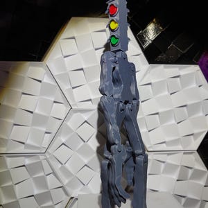 May include: A gray 3D printed articulated figure with a traffic light on top. The traffic light has red, yellow, and green lights.