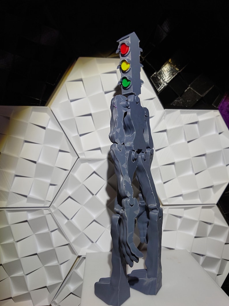 May include: A gray 3D printed articulated figure with a traffic light on top. The traffic light has red, yellow, and green lights.