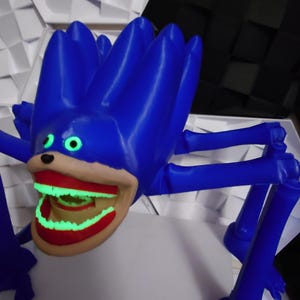 May include: A blue, spiky-haired creature with a large, open mouth revealing glowing green teeth. The creature has multiple blue legs and green eyes. The mouth is outlined in red. The overall design is cartoonish and whimsical.