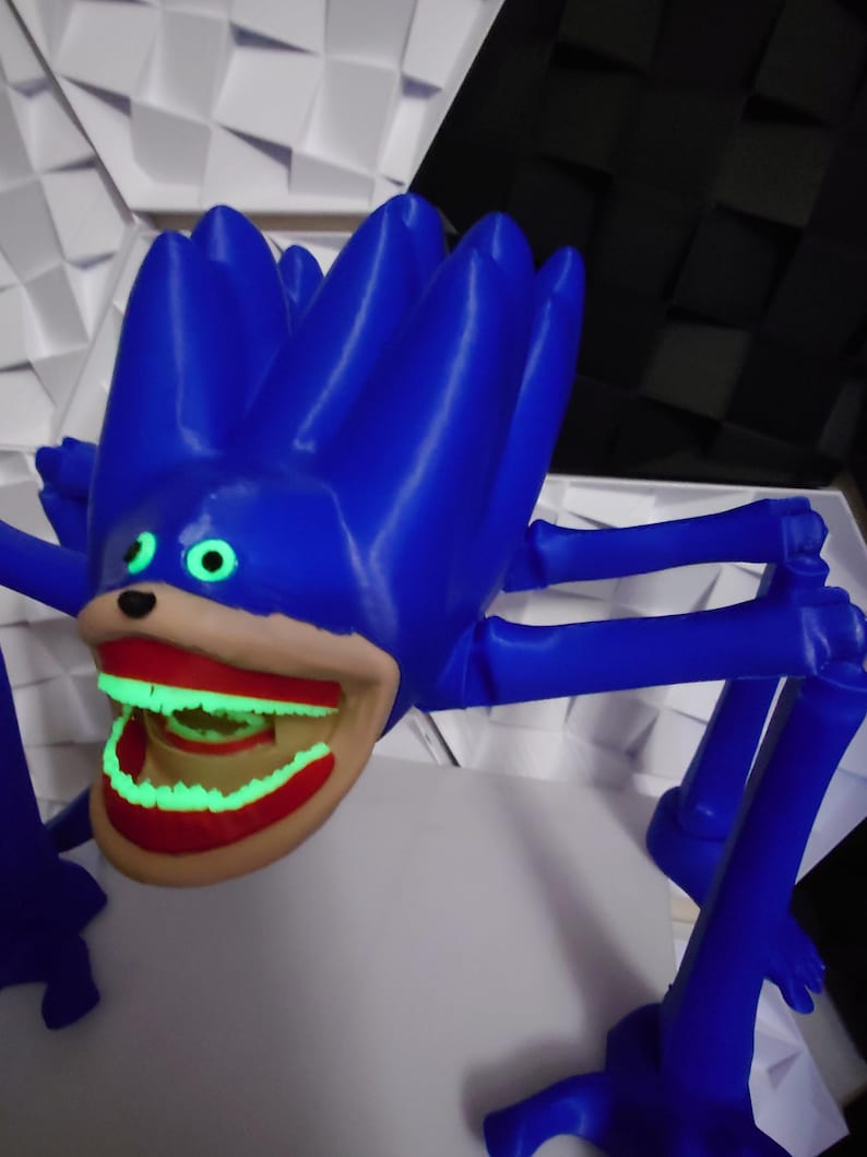 May include: A blue, spiky-haired creature with a large, open mouth revealing glowing green teeth. The creature has multiple blue legs and green eyes. The mouth is outlined in red. The overall design is cartoonish and whimsical.