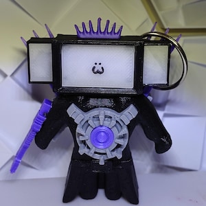 May include: A black and purple 3D printed keychain with a screen face and a crown on top. The screen has a simple smiley face on it. The keychain has a purple sword and a circular design on the chest.