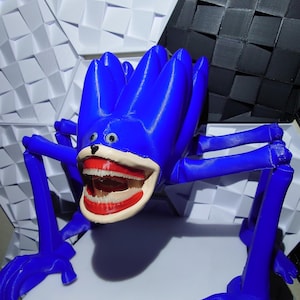 May include: A vibrant blue, 3D-printed sculpture of a creature with a large, open mouth revealing teeth and red lips. The sculpture has multiple legs and a flower-like head. The background features geometric shapes in white and black.