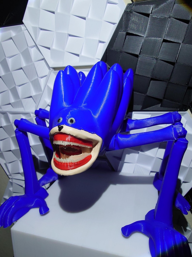 May include: A vibrant blue, 3D-printed sculpture of a creature with a large, open mouth revealing teeth and red lips. The sculpture has multiple legs and a flower-like head. The background features geometric shapes in white and black.