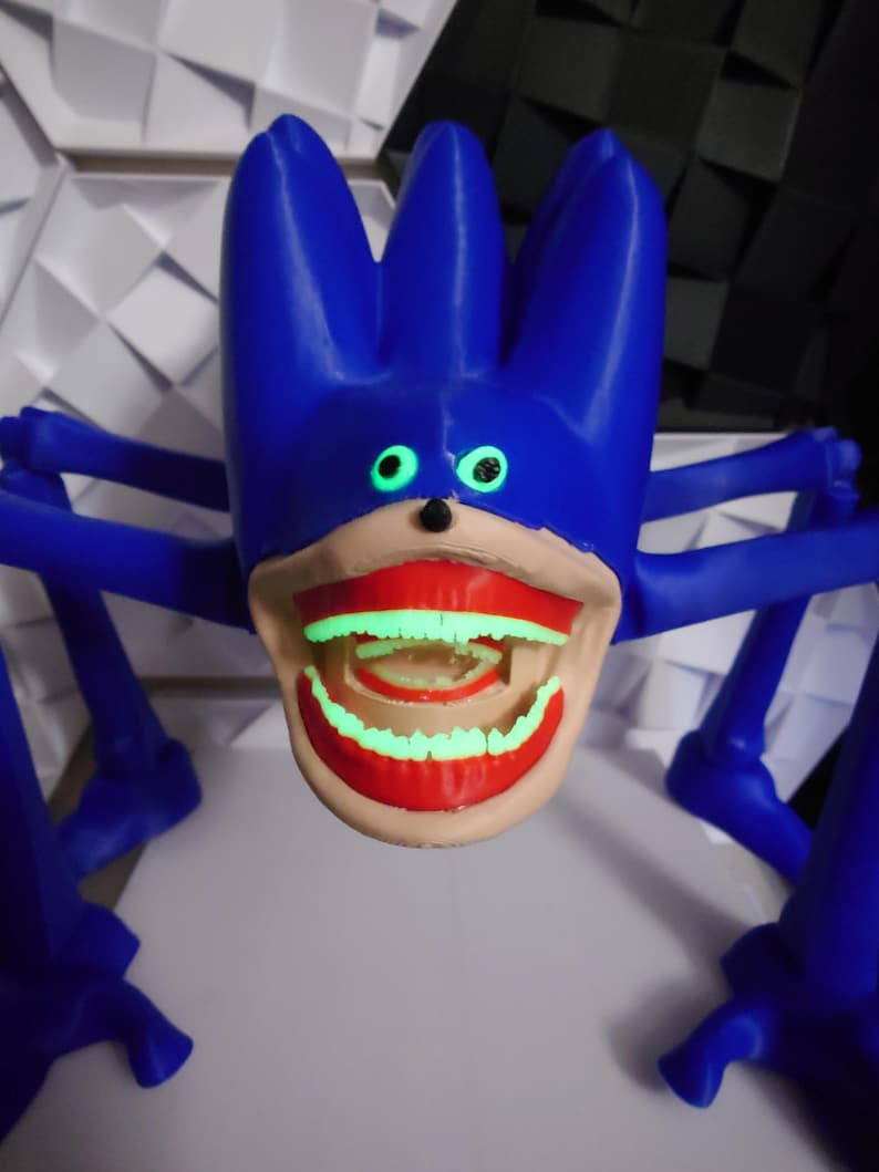 May include: A blue, spiky-haired creature with glowing green eyes and teeth. The creature has multiple blue legs and a large, open mouth with red lips. The teeth glow green, creating a striking contrast against the blue and tan colors.