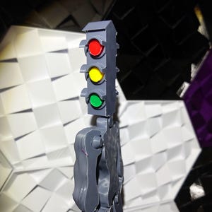 May include: A gray plastic toy figure with a traffic light head. The traffic light has red, yellow, and green lights.