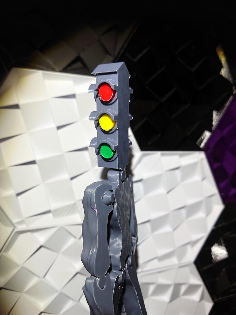 May include: A gray plastic toy figure with a traffic light head. The traffic light has red, yellow, and green lights.