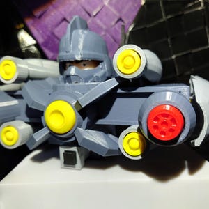 May include: A gray plastic toy robot with a helmet and multiple yellow and red cannons. The robot is posed with its cannons facing forward.