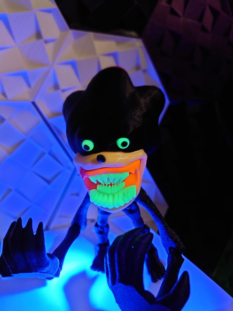 May include: A black and green toy figure with a large, toothy grin. The figure has glowing green eyes and teeth, and is posed with its arms outstretched.