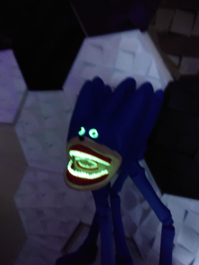 May include: A blue, monster-like figure with glowing green eyes and a wide, open mouth revealing glowing teeth. The figure has long, thin legs and a textured head. The background features geometric shapes.