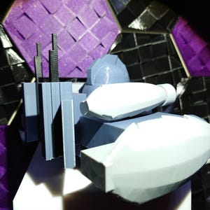 May include: A 3D printed model of a futuristic spaceship with a gray and white color scheme. The spaceship has a large, rounded front section and a smaller, rectangular rear section. There are several antennas on the top of the spaceship.