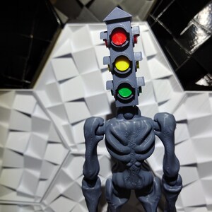 May include: A gray, skeletal figure with a traffic light for a head. The traffic light has red, yellow, and green lights. The figure is standing on a white, textured surface.