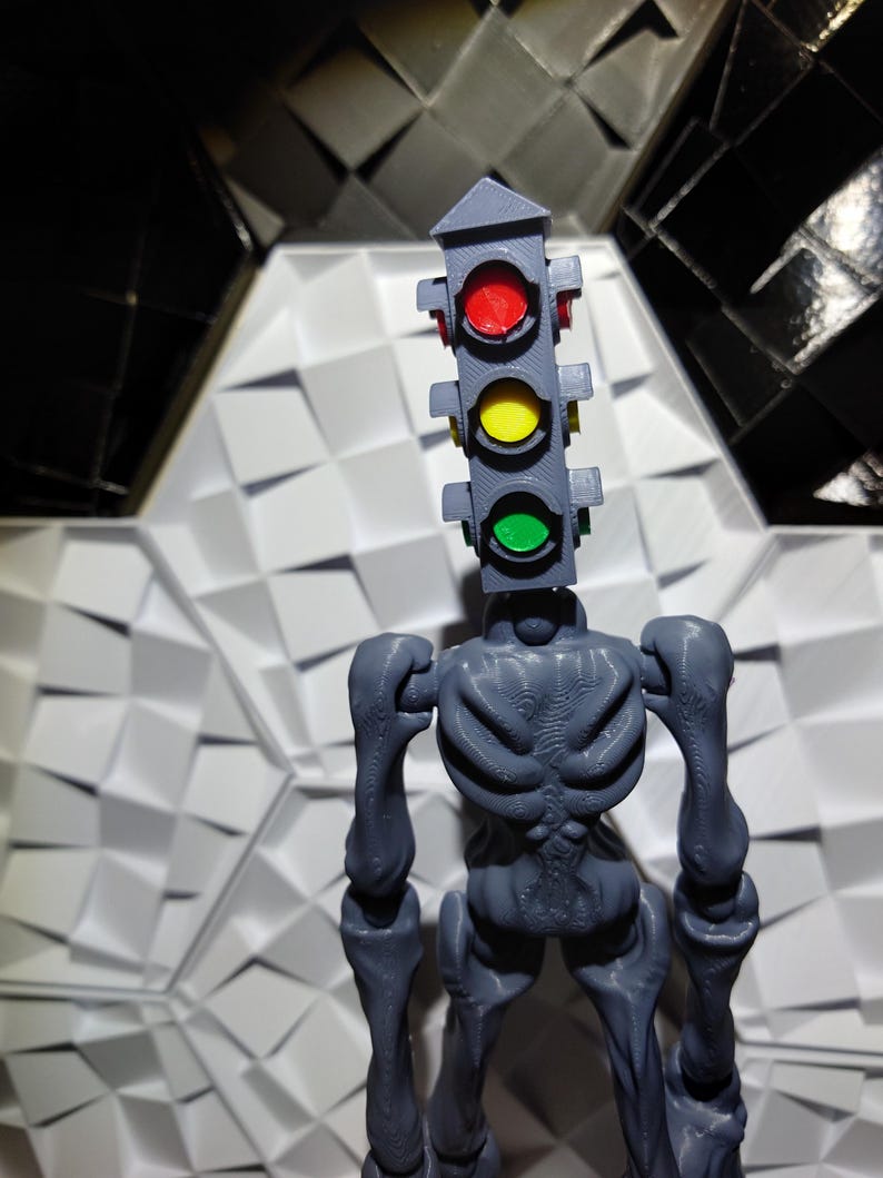 May include: A gray, skeletal figure with a traffic light for a head. The traffic light has red, yellow, and green lights. The figure is standing on a white, textured surface.