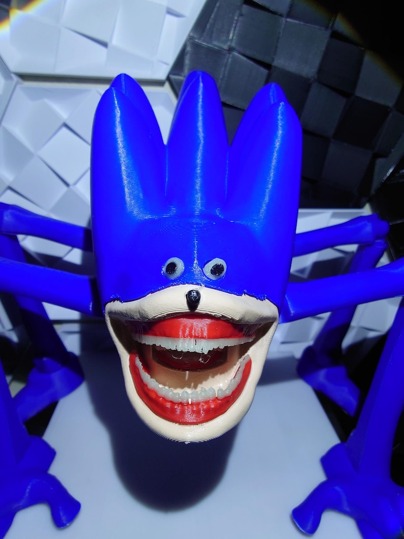 May include: A blue, 3D-printed sculpture of a cartoon character with a large, open mouth revealing teeth. The character has a blue head with three spikes, small eyes, and a black nose. The sculpture has multiple blue appendages extending from the head.