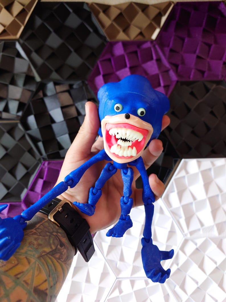 May include: A blue articulated toy figure of Sonic the Hedgehog with a wide, toothy grin and large, white eyes. The figure has multiple joints and is posed with its arms and legs outstretched.