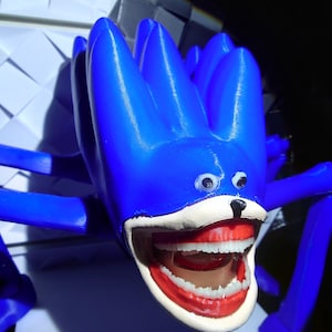May include: A blue, spiky, creature-like sculpture with a wide open mouth revealing white teeth and red gums. The sculpture has small, round eyes and a black nose. The overall design is whimsical and playful.