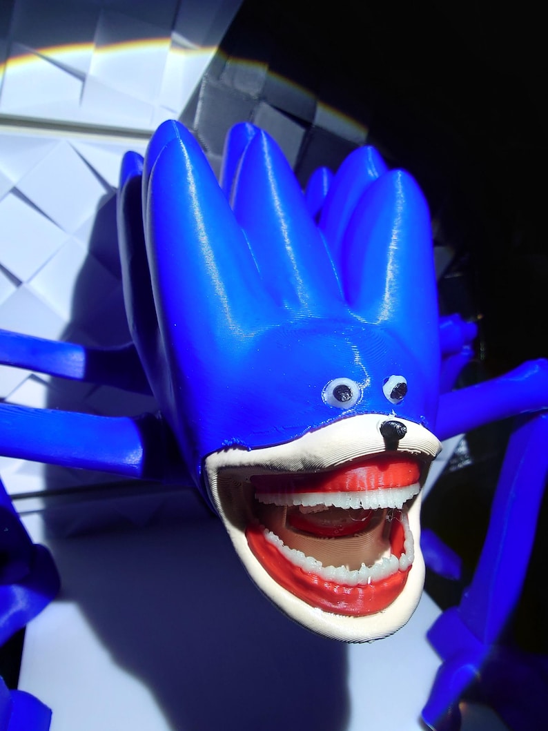 May include: A blue, spiky, creature-like sculpture with a wide open mouth revealing white teeth and red gums. The sculpture has small, round eyes and a black nose. The overall design is whimsical and playful.