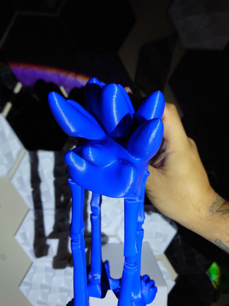 May include: A vibrant blue, 3D-printed sculpture of a stylized flower. The sculpture features a detailed floral design with elongated petals and stem-like supports. The piece is held in a hand, showcasing its size and form.