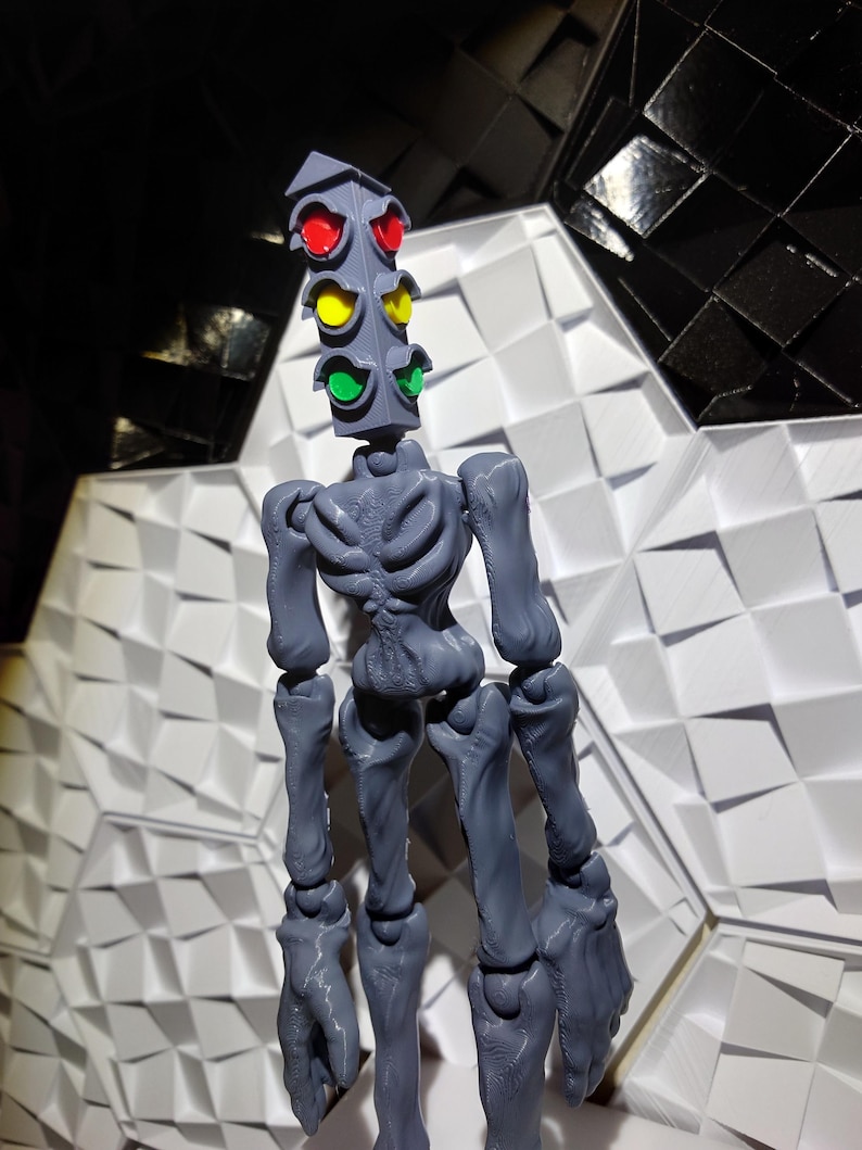 May include: A gray articulated figure with a traffic light for a head. The traffic light has red, yellow, and green lights. The figure is standing on a white and black patterned surface.