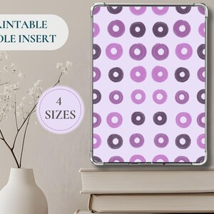 Può includere: Un inserto Kindle con un motivo ripetuto di cerchi viola e viola scuro su sfondo viola chiaro. È visibile anche il testo "PRINTABLE KINDLE INSERT" e "4 SIZES".