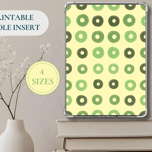 Può includere: Un inserto Kindle con un motivo ripetuto di cerchi verdi e verde scuro su sfondo giallo chiaro. Il testo "PRINTABLE KINDLE INSERT" è in alto a sinistra e un cerchio con "4 TAGLIE" al centro. L'inserto è esposto su una pila di libri.