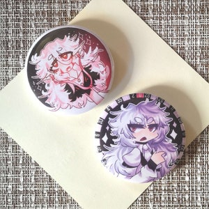 Può includere: Due spille rotonde con illustrazioni colorate in stile anime. La prima spilla presenta un personaggio con i capelli rosa che indossa un abito rosso e nero. La seconda spilla presenta un personaggio con i capelli bianchi che indossa un abito bianco e nero. Entrambe le spille hanno uno sfondo nero.