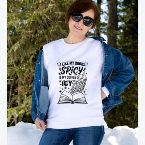 May include: White sweatshirt with the text "I LIKE MY BOOKS SPICY & MY COFFEE ICY". The graphic features a skeleton hand holding a coffee cup over an open book. The person is wearing a denim jacket and sunglasses.