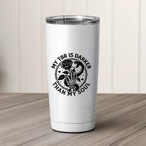 May include: White insulated tumbler with a black graphic. The graphic features a skeleton hand holding a rose and a snake, with the text "MY TBR IS DARKER THAN MY SOUL" in a circular design. The tumbler has a silver rim.