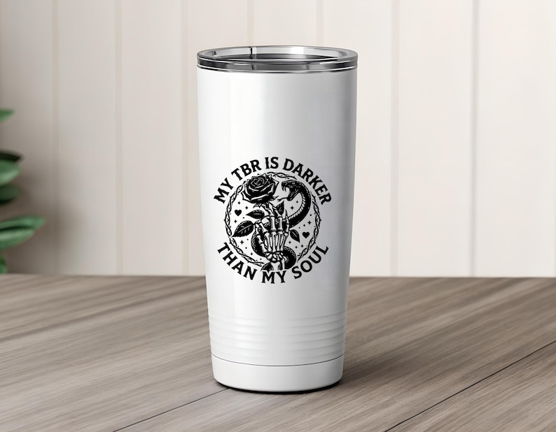 May include: White insulated tumbler with a black graphic. The graphic features a skeleton hand holding a rose and a snake, with the text "MY TBR IS DARKER THAN MY SOUL" in a circular design. The tumbler has a silver rim.