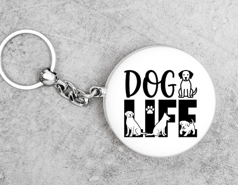 May include: White keychain with a round pendant featuring the words "DOG LIFE" in black, along with illustrations of three dogs and a paw print. The keychain has a silver ring and chain.